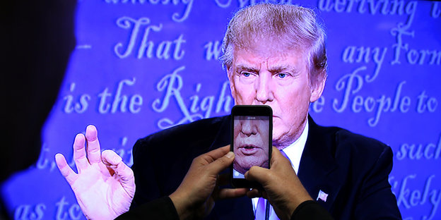 Ein Smartphone fotografiert Trumps Gesicht von einem Fernseher ab