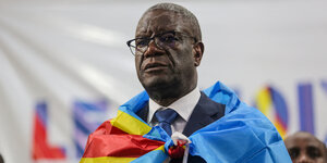 Denis Mukwege trägt die Falgge der Demokratischen Republik Kongo um dem Hals und schaut mit ernstem Gesicht nach vorne