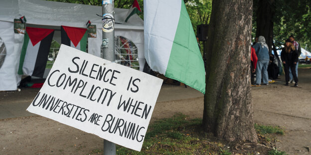 Ein weißes Zelt mit Palästina-Flaggen, davor ein Protest-Schild.