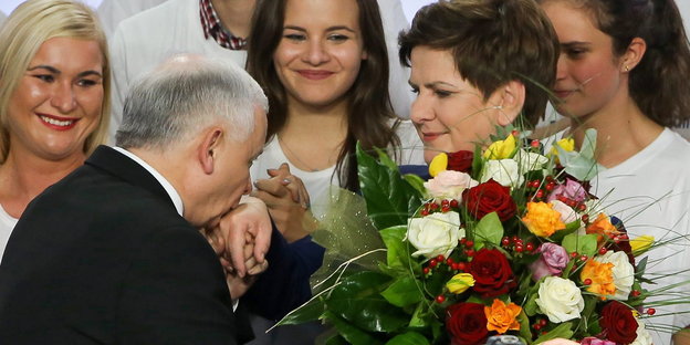 Kaczynski küsst die Hand von Szydlo, die einen Blumenstrauß trägt. .