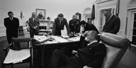 Ältere Herren stehen an einem Schreibtisch und schauen zu US-Präsident Lyndon B. Johnson
